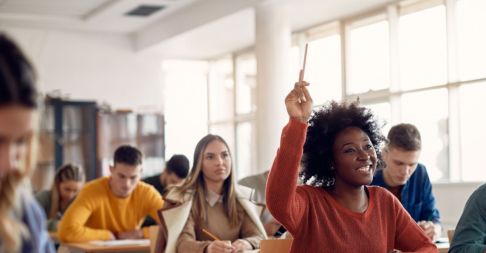 A student is raising their hand with a pencil in a classroom