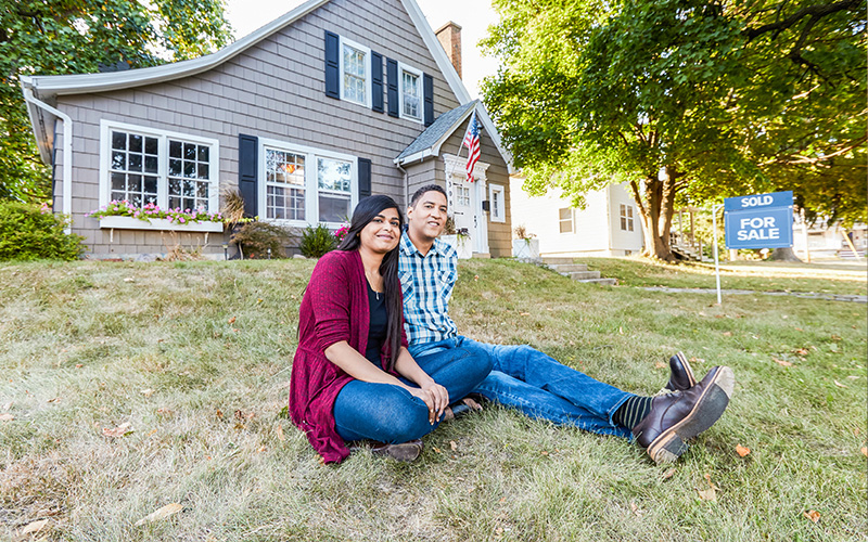 Couple sitting in front of house on grass