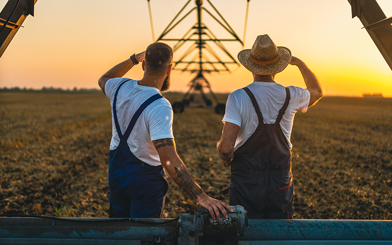 Two farmers overlooking field and irrigation system.