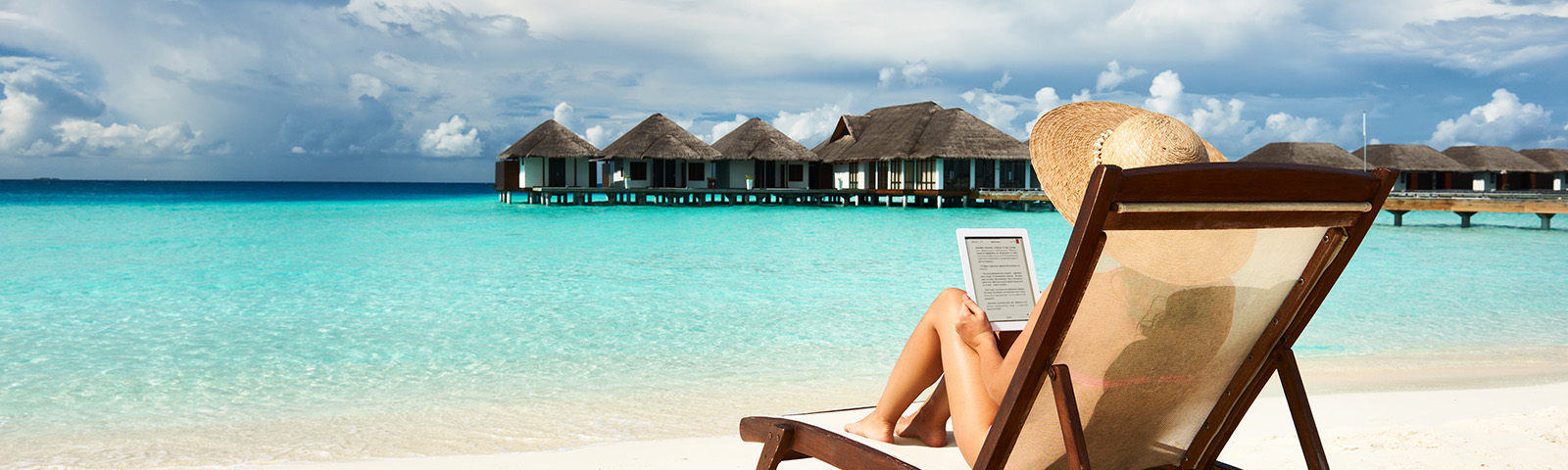 a person lounging on a beach in a chair reading her tablet.