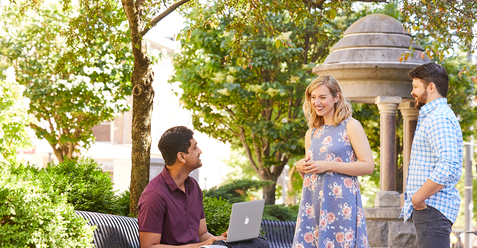 man on a bench with a laptop with two people smiling at him