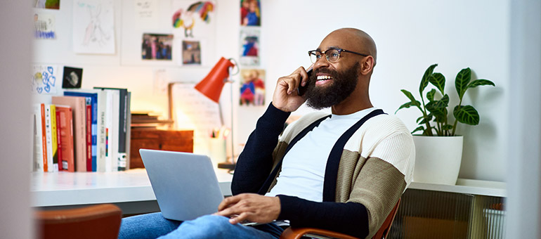 a man siting in a chair smiling with a laptop in his lap while on the phone