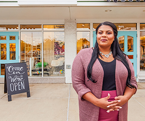 A business woman in front of her store with the sign of Come in, We're Open.